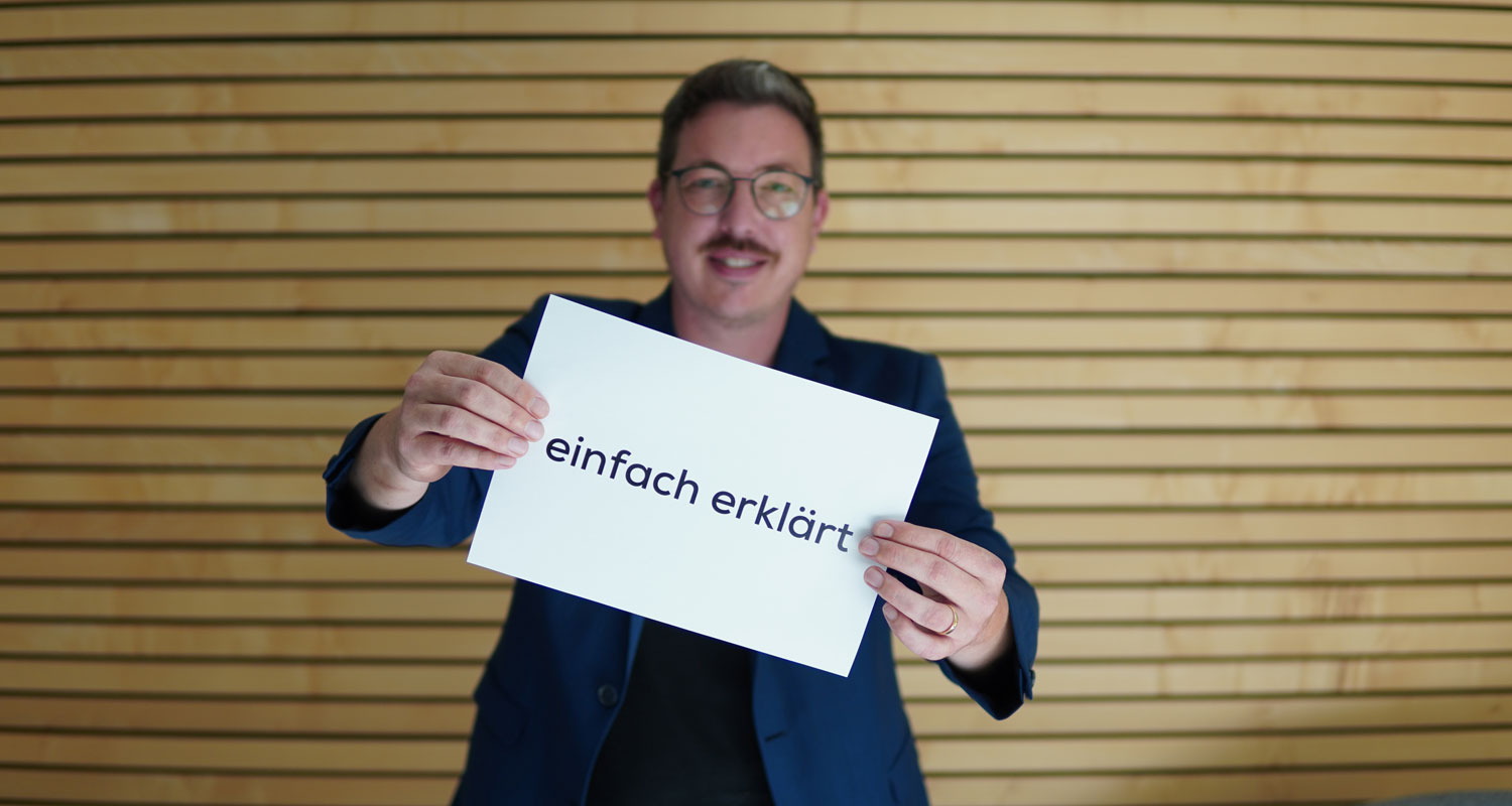 Michael Jansen hält ein Blatt Papier mit den Worten "einfach erklärt" in die Kamera