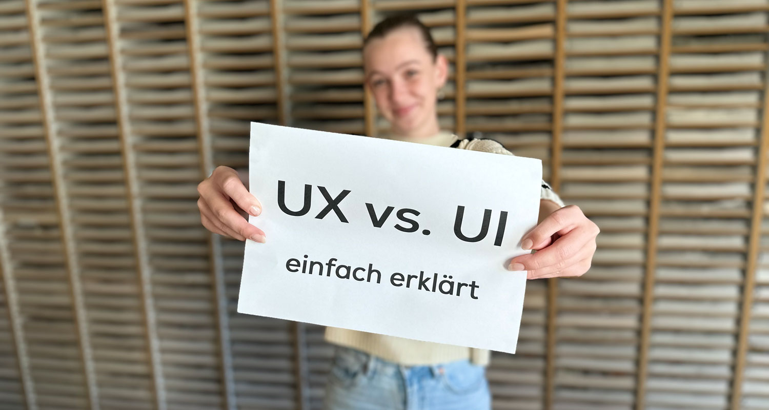 Eine Frau mit einem Zettel in der Hand auf dem "UX vs. UI - einfach erklärt" steht