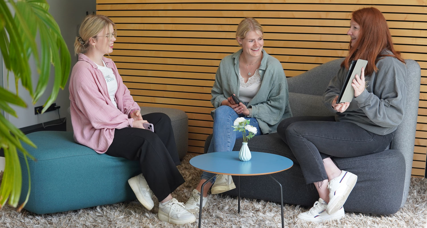 Drei Frauen sitzen auf einem Sofa, interagieren miteinander. Eine Frau hält ein Tablet in der Hand